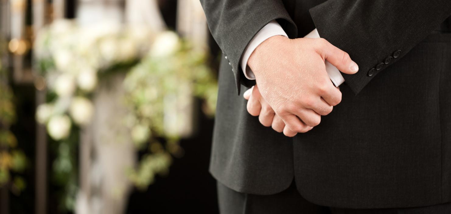 Ein Mann in einem Anzug steht mit verschränkten Händen vor einer dekorierten Kulisse mit Blumen und Kerzen.