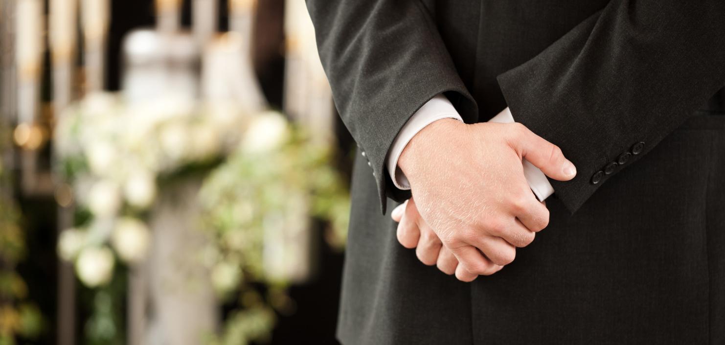 Ein Mann in einem Anzug steht mit verschränkten Händen vor einer dekorierten Kulisse mit Blumen und Kerzen.